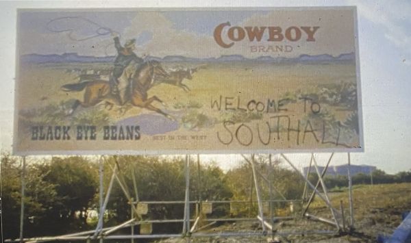 Billboard with cowboy on a horse holding a lasso. The top right says “Cowboy brand.” “Welcome to Southall” is spray-painted on the bottom right.